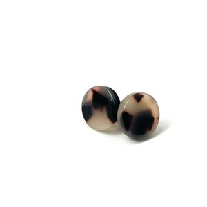 May include: A pair of small, round earrings with a black and white tortoiseshell pattern.