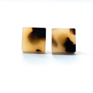 May include: A pair of square-shaped earrings with a tortoiseshell pattern. The earrings are a light brown color with dark brown swirls.