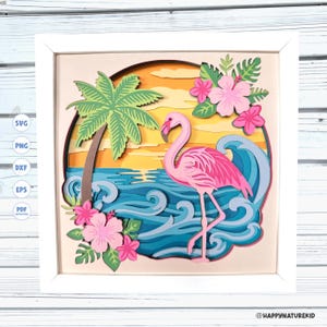 May include: A layered paper art piece in a white frame featuring a pink flamingo standing in blue ocean waves. The scene includes a green palm tree, yellow sunset sky, and pink hibiscus flowers. Text on the left lists SVG, PNG, DXF, EPS, PDF.
