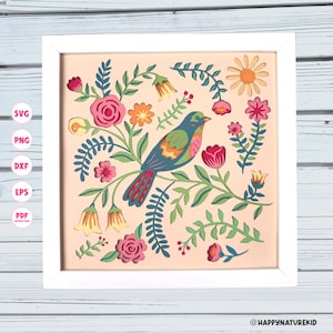 May include: A framed, colorful paper cut art piece featuring a bird perched on a branch surrounded by flowers and foliage. The bird has blue, green, and red details. The artwork is in a white frame.