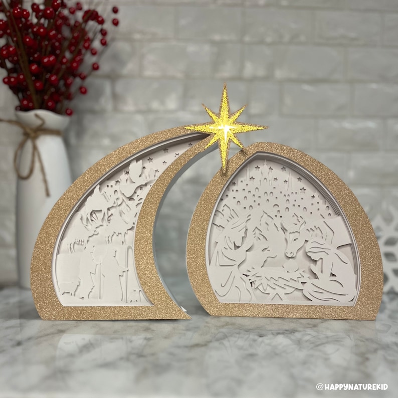 May include: A gold glitter-covered wooden nativity scene with a star on top. The scene depicts the birth of Jesus with Mary, Joseph, and a donkey.