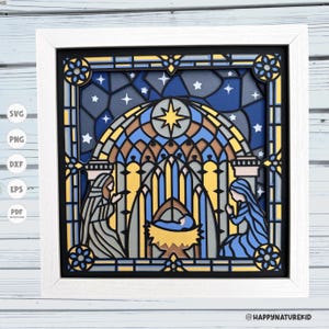May include: A stained glass style papercraft design featuring the nativity scene. The design includes a blue and gold star, a manger with a baby, Mary and Joseph, and a blue night sky with white stars.
