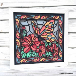 May include: A white framed wall art piece with a black background featuring a colorful butterfly and flowers. The butterfly is red, yellow, and blue with black outlines. The flowers are red with green leaves. The frame has a decorative border with swirls and lines in orange, yellow, and blue.
