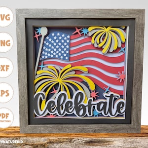 May include: A framed paper craft with a red, white, and blue American flag, yellow and gray fireworks, and the word "Celebrate" in black lettering.