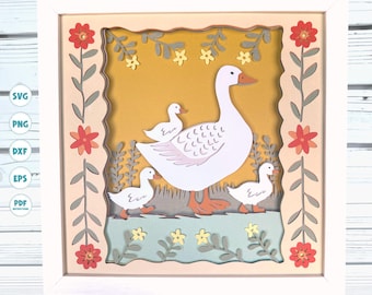 May include: A white goose with three baby geese in a layered paper craft frame. The frame has a yellow background with green leaves and flowers. The geese are walking on a green and blue water scene.