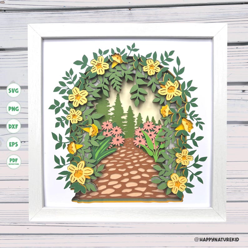 May include: A papercraft scene of a path through a forest, framed in white. The path is made of brown paper and leads to a forest of green trees. The path is surrounded by yellow flowers and green leaves.