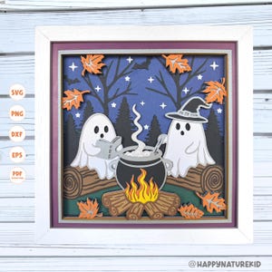 Puede incluir: Una obra de arte en papel enmarcada con temática de Halloween. Dos fantasmas blancos se reúnen alrededor de un caldero, con una fogata debajo. El fondo es una escena nocturna azul oscuro con árboles, estrellas y hojas naranjas. El marco es blanco.