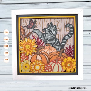 May include: A framed paper art piece depicting a grey tabby cat and a butterfly, surrounded by pumpkins, sunflowers, and autumn leaves. The artwork is layered, creating a 3D effect, and is set within a white frame.