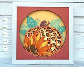 May include: A framed paper art piece featuring a layered pumpkin design. The pumpkin has a leopard print pattern and a sunflower in the center. The artwork includes teal leaves and is set against a warm orange and yellow background.