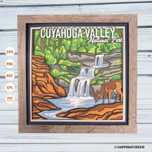 May include: A framed, layered paper art piece depicting Cuyahoga Valley National Park. The artwork features a waterfall, a deer, and the park's name. The frame is a light brown color, and the artwork has a 3D effect.