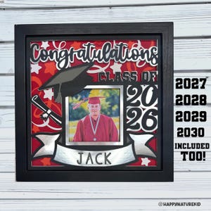 Può includere: Una cornice nera per una scatola ombra di laurea con le parole "Congratulations Class of 2026" in argento. La scatola include una foto di un laureato, un cappello di laurea e un diploma. Il nome "Jack" è visualizzato su uno striscione.
