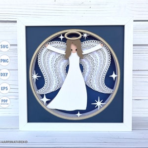 May include: A white paper angel with a halo and wings, against a blue background with white stars. The angel is in a round frame with a gold border.