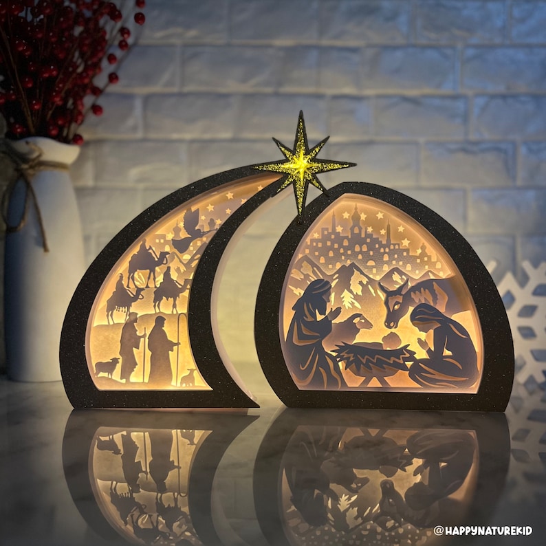 May include: A wooden Christmas nativity scene with a black glitter finish. The scene depicts the birth of Jesus with Mary, Joseph, and a donkey. The scene is illuminated with warm white LED lights. The scene is set against a backdrop of a crescent moon and a star.