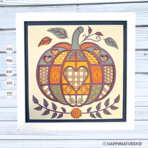 May include: A layered paper art piece featuring a pumpkin design in a white frame. The pumpkin is orange, yellow, and purple with heart and floral cutouts. Green leaves and a sunflower accent the design. The text "@HAPPY NATURE KID" is visible.