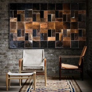 Könnte beinhalten: Zwei Stühle mit Holzrahmen und Ledersitzen, einer mit einer Leinwandlehne und einem Fußhocker, vor einer Wand mit einem großen Patchwork aus braunen und schwarzen Lederquadraten.