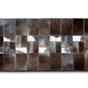 Può includere: Un tappeto patchwork in pelle di mucca in tonalità di marrone, grigio e bianco. Il tappeto è composto da quadrati di diverse dimensioni e cucito con filo nero.
