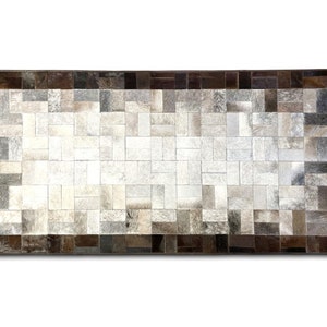 Könnte beinhalten: Ein rechteckiger Kuhfellteppich mit Patchwork-Muster. Der Teppich besteht aus kleinen Quadraten aus verschiedenen Brauntönen und weißem Kuhfell. Der Teppich hat einen dunkelbraunen Rand.
