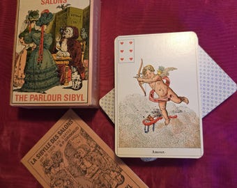 May include: A vintage tarot card deck titled "The Parlour Sibyl" with illustrations. The deck includes a box, a card with an image of Cupid, and a booklet. The box and booklet feature illustrations of people in period clothing.