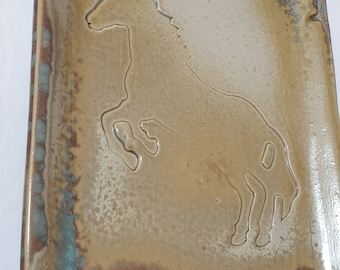 Może przedstawiać: Prostokątna ceramiczna taca do serwowania z jasnobrązową glazurą i turkusową glazurą wokół krawędzi. Taca ma wypukły zarys konia w środku.