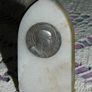 Peut inclure: Une plaque en marbre blanc avec une pièce d'argent représentant un profil de femme. La pièce porte l'inscription "S. LUCIA" sur le bord.