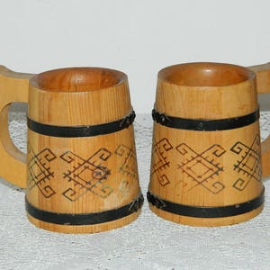Peut inclure: Deux chopes en bois avec des bandes métalliques noires et un motif géométrique gravé dans le bois.