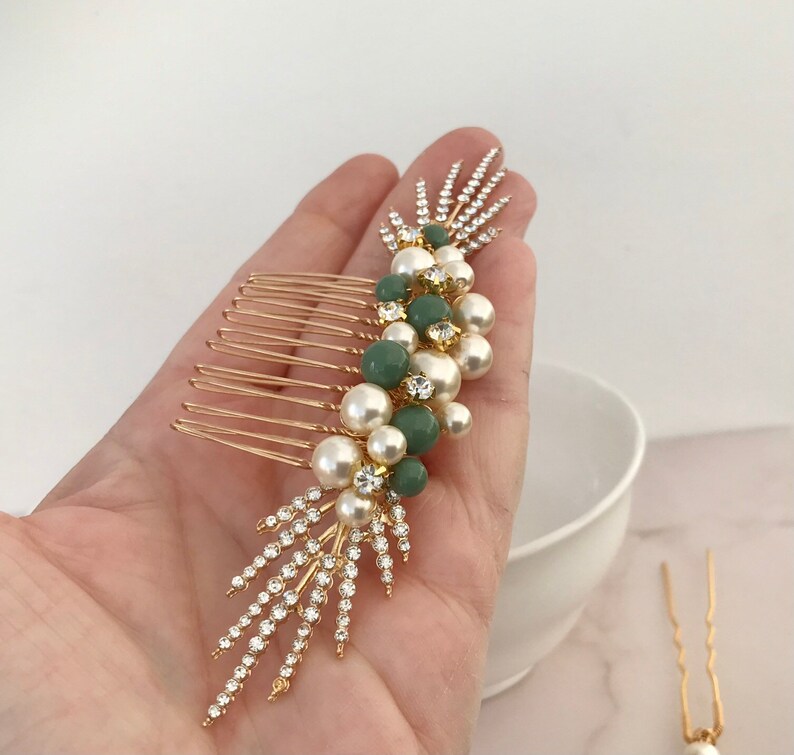 K&ouml;nnte beinhalten: Goldener Haarkamm mit einem Cluster aus Kunstperlen und gr&uuml;nen Steinen. Der Kamm hat ein dekoratives Design mit Strasssteinen.