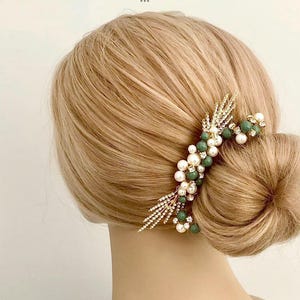K&ouml;nnte beinhalten: Goldener Haarkamm mit gr&uuml;nen und wei&szlig;en Perlen. Der Kamm hat ein zartes, blattf&ouml;rmiges Design und ist perfekt, um jeder Frisur einen Hauch von Eleganz zu verleihen.