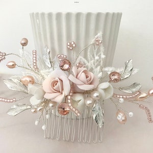 K&ouml;nnte beinhalten: Ein silberner Haarkamm mit einem bl&auml;ulich-rosa und wei&szlig;en Blumendesign. Der Kamm ist mit Perlen, Perlen und silbernen Bl&auml;ttern verziert.