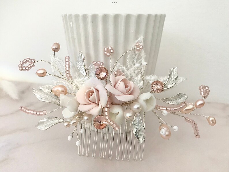 K&ouml;nnte beinhalten: Ein silberner Haarkamm mit einem bl&auml;ulich-rosa und wei&szlig;en Blumendesign. Der Kamm ist mit Perlen, Perlen und silbernen Bl&auml;ttern verziert.