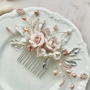 K&ouml;nnte beinhalten: Ein zarter Haarkamm mit zartrosa und wei&szlig;en Bl&uuml;ten, silbernen Bl&auml;ttern und Perlen sowie ros&eacute;goldenen Perlen. Der Kamm ist perfekt f&uuml;r eine Hochzeit oder einen besonderen Anlass.