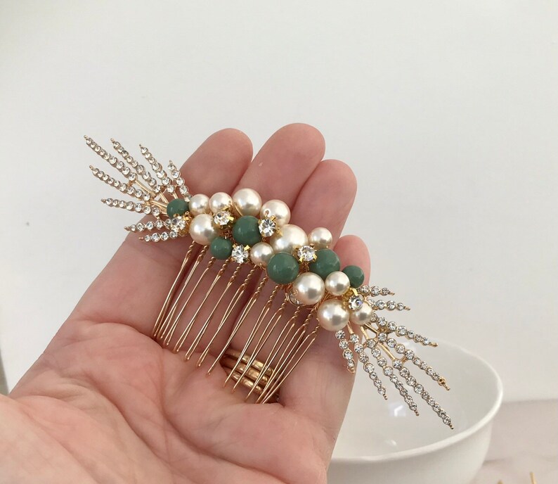 K&ouml;nnte beinhalten: Goldener Haarkamm mit einem Cluster aus Kunstperlen und gr&uuml;nen Perlen, akzentuiert mit Strasssteinen. Der Kamm hat ein dekoratives, blattf&ouml;rmiges Design.