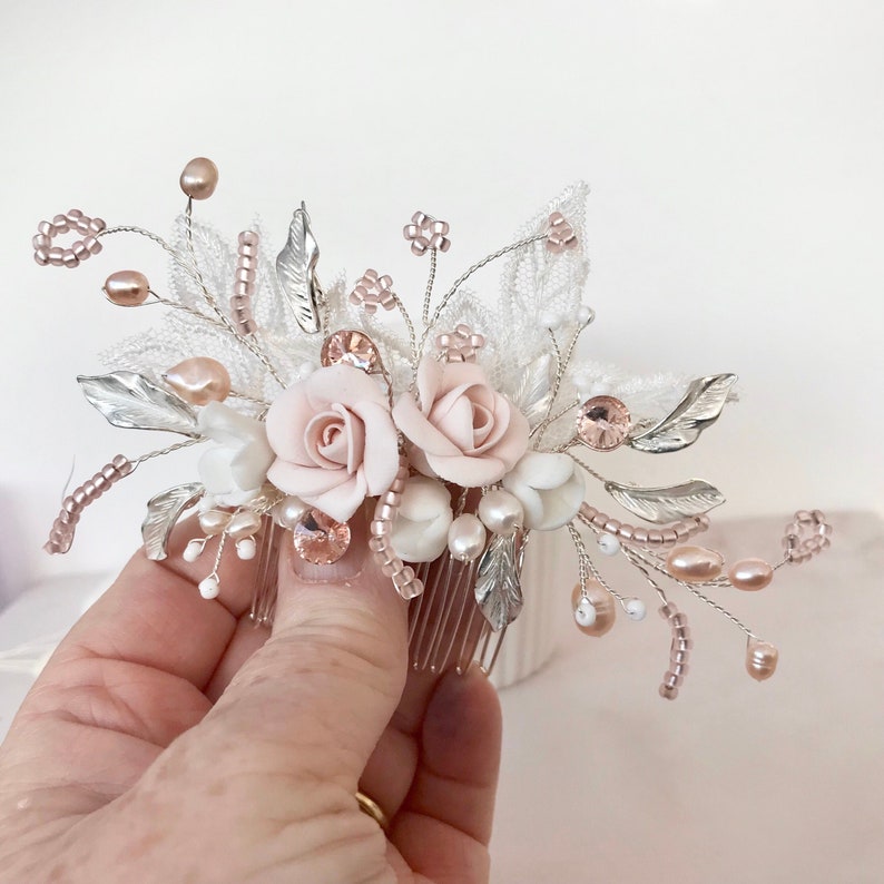 K&ouml;nnte beinhalten: Ein rosafarbener und wei&szlig;er Blumenhaarkamm mit silbernen und ros&eacute;goldenen Akzenten. Der Kamm hat zwei rosafarbene Rosen, wei&szlig;e Perlen und silberne Bl&auml;tter.