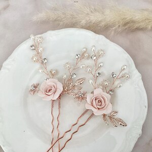 May include: Three rose gold hair pins with pink fabric roses and pearl and crystal embellishments.