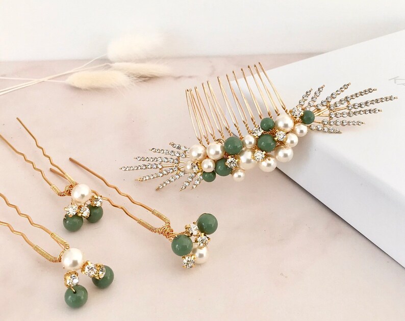 K&ouml;nnte beinhalten: Ein Set aus drei goldenen Haark&auml;mmen mit gr&uuml;nen und wei&szlig;en Perlenakzenten. Der gr&ouml;&szlig;te Kamm hat ein dekoratives Design mit einem Cluster aus Perlen und gr&uuml;nen Perlen. Die beiden kleineren K&auml;mme sind Haarnadeln mit einem Cluster aus Perlen und gr&uuml;nen Perlen.