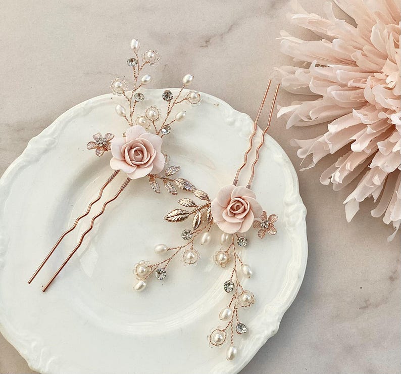 May include: Two gold hair pins with delicate floral designs. Each pin features a blush pink flower with pearl and crystal accents.