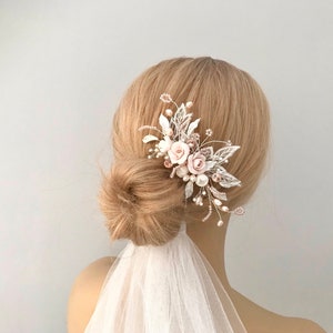 K&ouml;nnte beinhalten: Ein zarter Braut-Haarkamm mit zartrosa Bl&uuml;ten, silbernen Bl&auml;ttern und Perlenakzenten. Der Kamm ist f&uuml;r eine Hochzeit oder einen besonderen Anlass gedacht.
