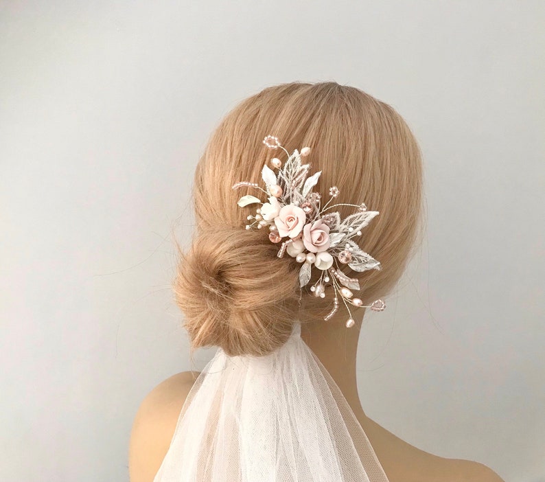 K&ouml;nnte beinhalten: Ein zarter Braut-Haarkamm mit zartrosa Bl&uuml;ten, silbernen Bl&auml;ttern und Perlenakzenten. Der Kamm ist f&uuml;r eine Hochzeit oder einen besonderen Anlass gedacht.