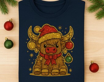 May include: Navy blue t-shirt featuring a glittery illustration of a Highland cow wearing a Santa hat and a red bow. The cow has golden horns and is decorated with Christmas ornaments. A festive holiday design.