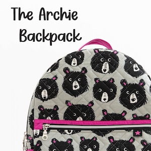 May include: A gray quilted backpack with a black bear print and pink accents. The backpack has a zippered pocket and a small pocket on the side. The backpack has a pink label that says "Knot + Thread design".