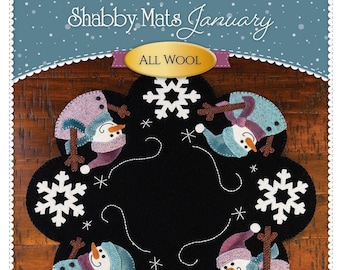 May include: A black felt Christmas ornament with a snowflake and snowman design. The ornament is made of wool and has a pink, blue, and white color scheme. The text "Shabby Mats January" and "All Wool" is visible on the ornament. The text "Shabby Fabrics.com" is also visible on the ornament.