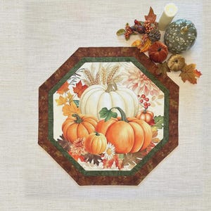 May include: An octagonal table topper with a fall theme, featuring pumpkins and autumn leaves. The text "Playing with Panels Table Topper" is at the top. Finished size is 24 1/2" x 24 1/2".