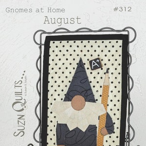 May include: A black and white fabric gnome with a red hat and a pencil in its hand. The gnome is holding a small chalkboard with an A+ on it. The fabric is on a black frame with a white background. The text "Gnomes at Home #312 August" is at the top of the image. The text "Fabrics by Moda" is at the bottom of the image. The text "Sewing with Susan 6" x 9" is in the bottom right corner of the image.
