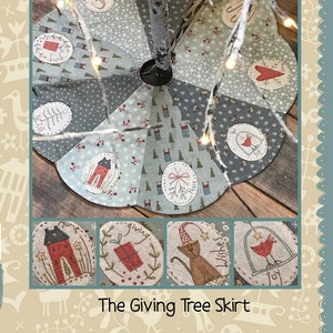 May include: A handmade Christmas tree skirt with a patchwork design featuring various holiday themes. The skirt is made of a light blue fabric with white snowflakes and red birds. The skirt is decorated with appliques of a house, a gift, a cat, and a bird in a cage. The skirt is titled "The Giving Tree Skirt" and is made by "Hatched and Patched".