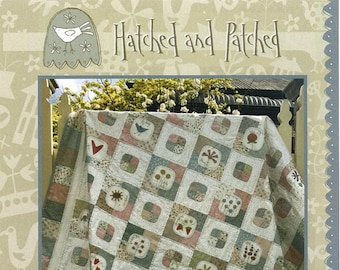 May include: A quilt pattern featuring a patchwork design with a variety of floral and nature-inspired motifs. The quilt is displayed on a wooden fence with a green lawn in the background. The quilt is titled "Market Garden Quilt" and is part of the "Hatched and Patched" collection.