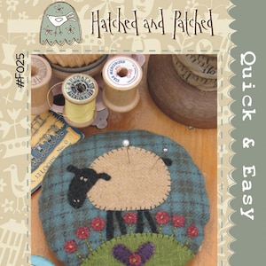 May include: A handmade pincushion featuring a sheep design with a tan body, black head, and legs, set against a teal background. The sheep is surrounded by red flowers and a purple heart. The text "Larry Lamb Pincushion" is at the bottom.
