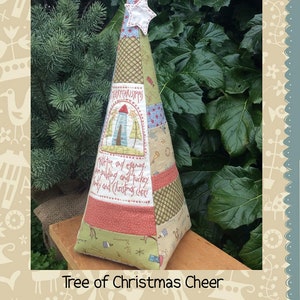 May include: A handmade Christmas tree-shaped pillow with a patchwork design. The pillow is made of various fabrics in shades of green, red, and blue. The pillow features a star-shaped embellishment and the text "Merry Christmas" and "Mince pie for and eggnog, plum pudding and turkey, holly and Christmas cheer".