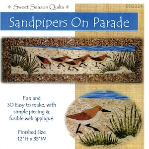 May include: A quilting pattern for a wall hanging featuring sandpipers on a beach. The pattern is titled "Sandpipers On Parade" and is from the series "Over East" by Sue Pritt. The finished size is 12 inches high by 35 inches wide.