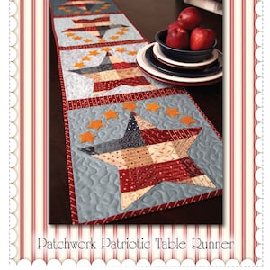May include: A patchwork table runner with a patriotic theme. The runner features a blue background with five red, white, and blue stars. The stars are surrounded by orange stars. The runner is on a dark wood table with a bowl of red apples and plates.