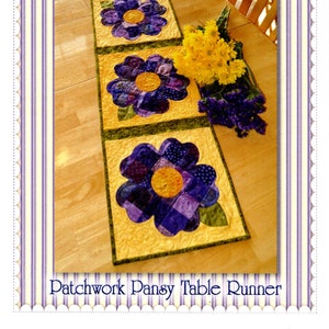 May include: A patchwork pansy table runner with four purple and yellow flowers on a yellow background. The table runner is on a wooden table with a bouquet of yellow flowers and lavender.