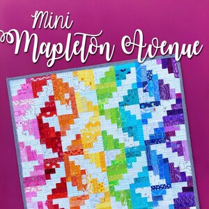 May include: A colorful rainbow quilt with a white background and a black and white striped border. The quilt is titled "Mini Mapleton Avenue".